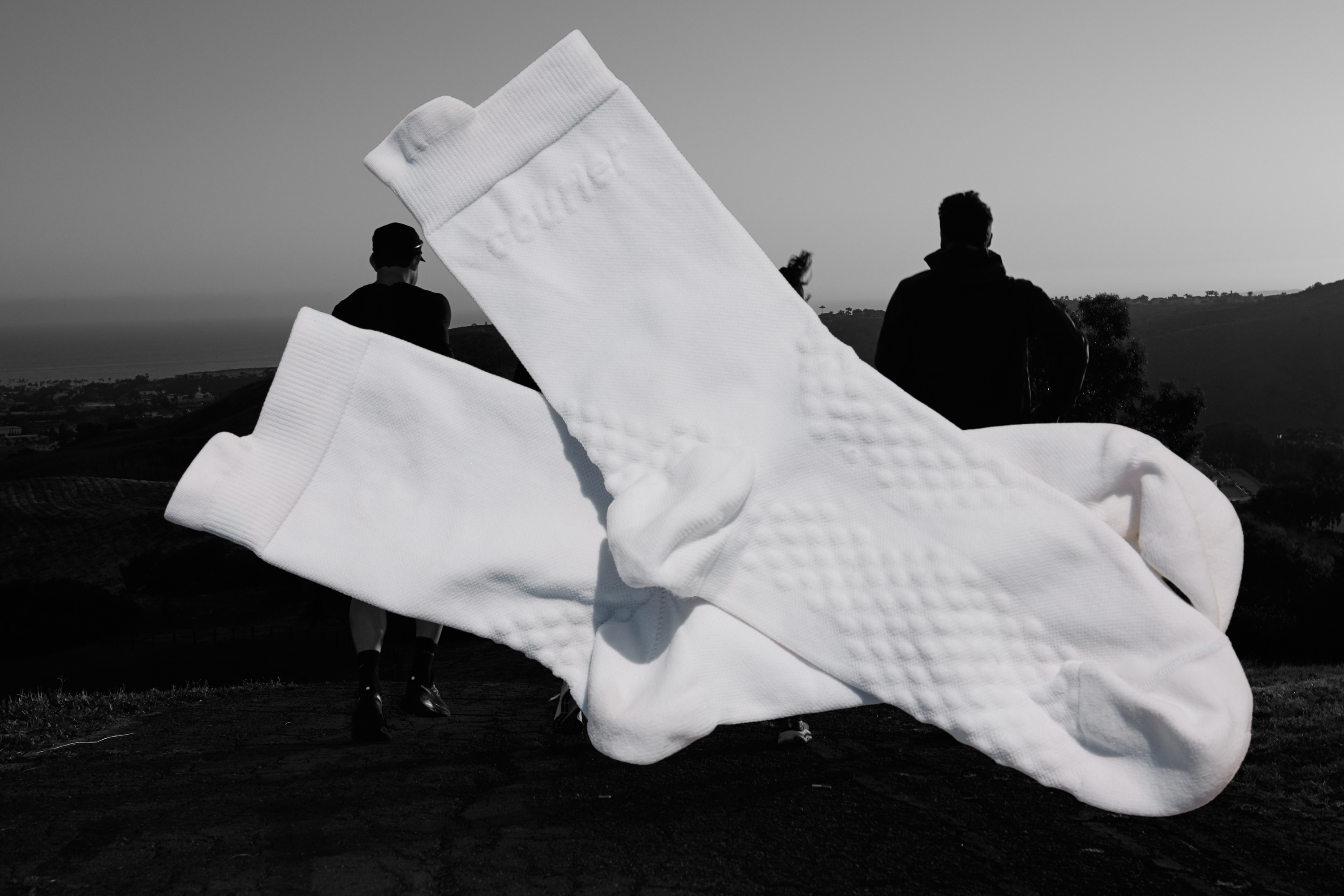 Close up of Courier HiFi socks in white, lay flat superimposed onto background with marathon runners